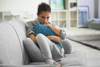 Depressive junge Frau kauert auf dem Sofa