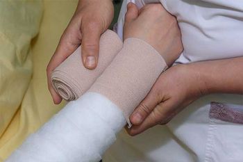 Lymphödem-Behandlung: Frau bandagiert Arm einer Brustkrebs-Patientin