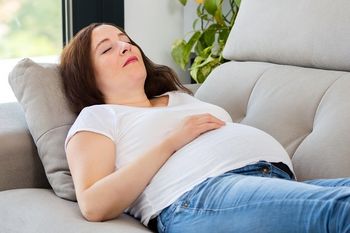 Hochschwangere Frau döst auf dem Sofa