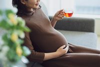 Hochschwangere Frau sitzt auf dem Sofa und genießt eine Tasse Tee