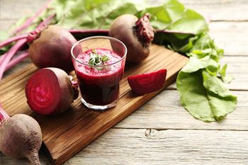 Ein Glas Rote-Bete-Saft und Knollen auf einem Holzbrett