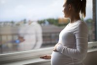 Schwangere junge Frau blickt nachdenklich aus dem Fenster