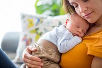 Junge Mutter kuschelt mit ihrem schlafenden Baby
