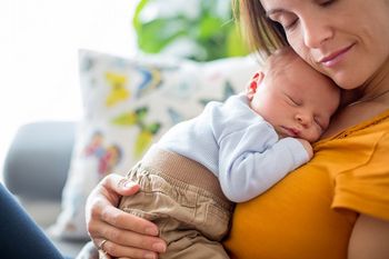 Junge Mutter kuschelt mit ihrem schlafenden Baby