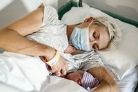 Mutter mit Mund-Nasen-Schutz stillt ihr Neugeborenes