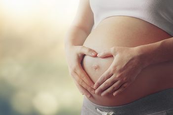 Schwangere, die mit ihren H&auml;nden ein Herz auf ihrem Babybauch formt
