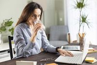 Junge Frau trinkt Wasser, während sie am Laptop arbeitet