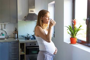 Schwangere trinkt in der Küche Wasser und blickt aus dem Fenster
