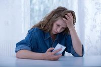 Junge Frau blickt ängstlich auf ihr Smartphone