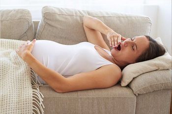 Müde Schwangere liegt auf dem Sofa und gähnt