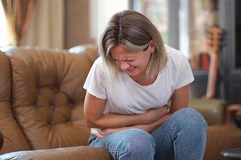 Unterleibskrampf: Frau krümmt sich vor Schmerzen auf dem Sofa