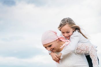 Lächelnde krebskranke Frau trägt Tochter huckepack