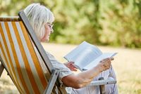 Seniorin sitzt im Freien und liest ein Buch